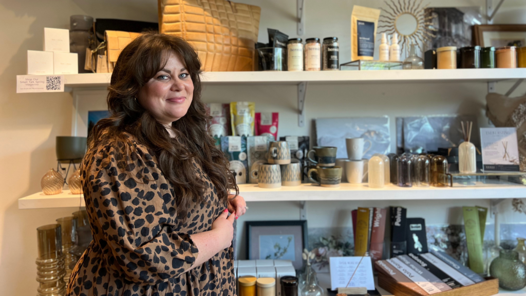 Let's celebrate woman with Calli, the owner of Far and Wide, standing in front of a shelf full of products