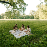 People sitting under a big tree hosting a garden party that is Bridgerton inspired