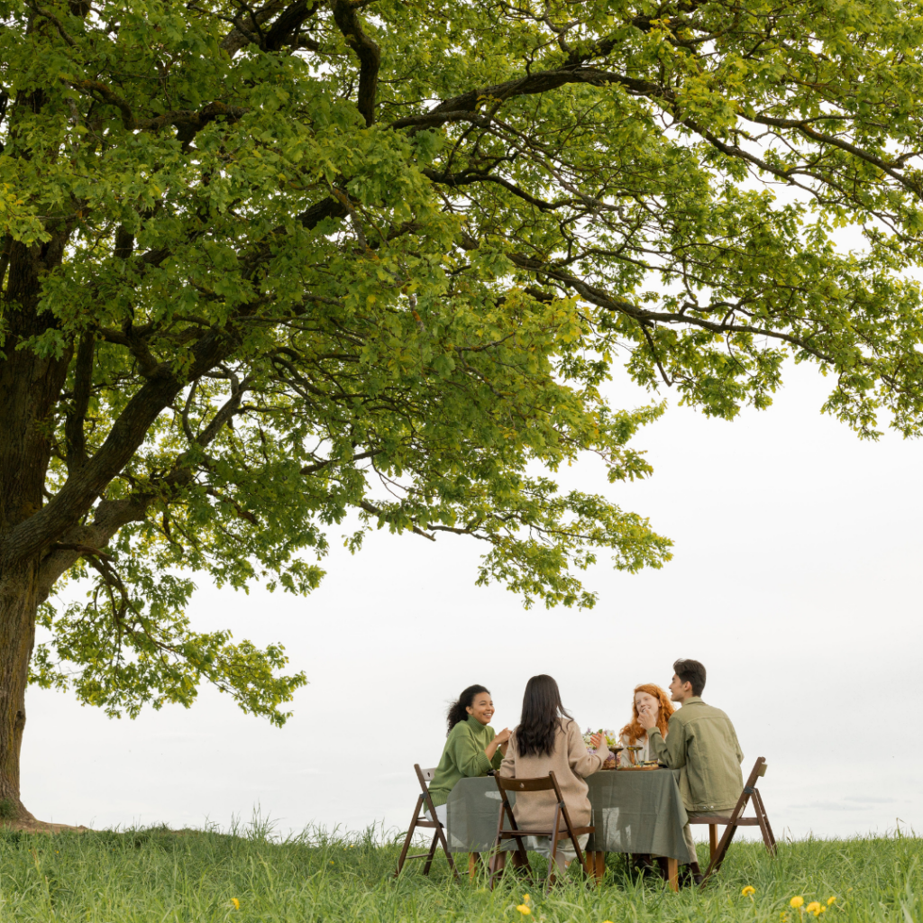 People sitting under a big tree hosting a garden party that is Bridgerton inspired